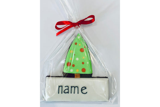 personalised biscuit name place setting. Iced green Christmas tree with name iced in black icing below. Wrapped in cellophane and tied with red ribbon.
