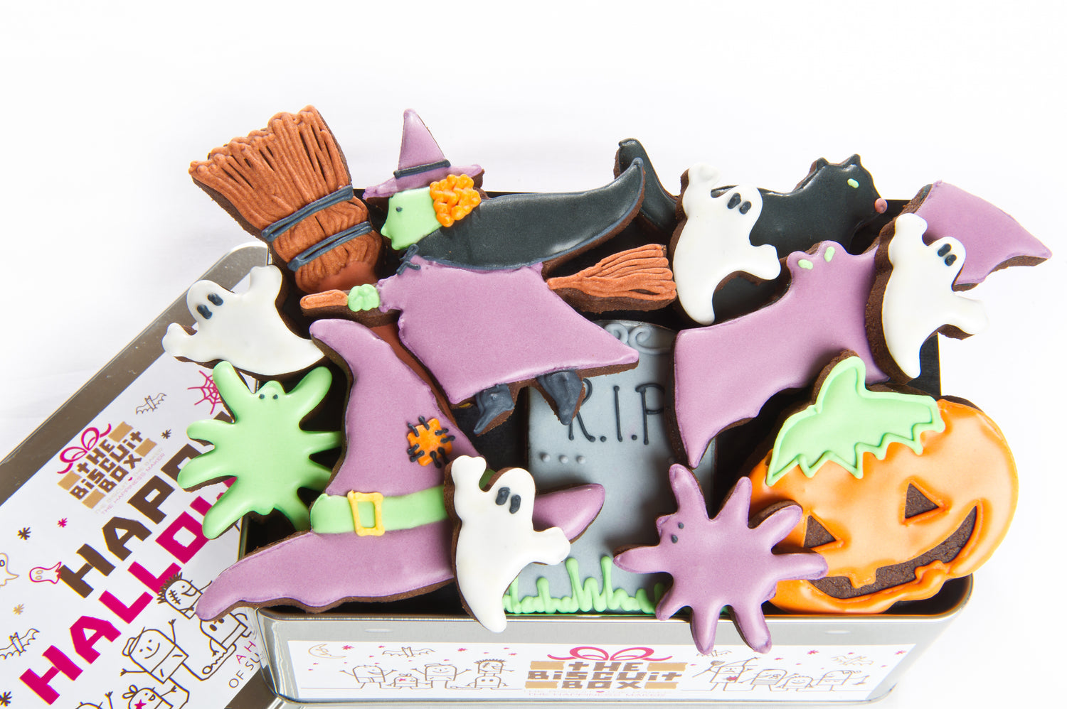 biscuit tin packed with hand iced Halloween biscuits. iced pumpkin, purple bat biscuit. whitches hat and gravestone. Flying witch biscuit, happy halloween biscuits