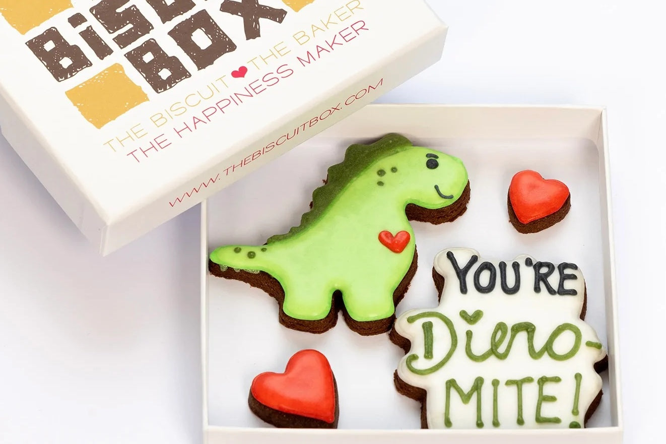 Valentines biscuit box with a dinosaur theme. Green dinosaur and text biscuit that says you are dino-mite. Red heart cookie.