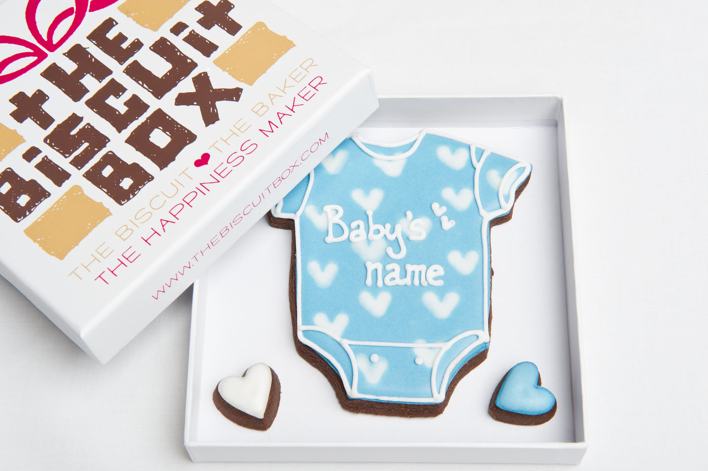 baby vest with iced blue and white hearts with baby's name iced onto it shown in biscuit card packaging